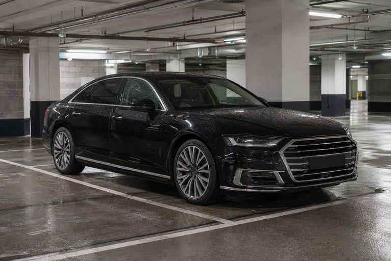 A black executive saloon with rain on its bonnet, parked in an underground car park.