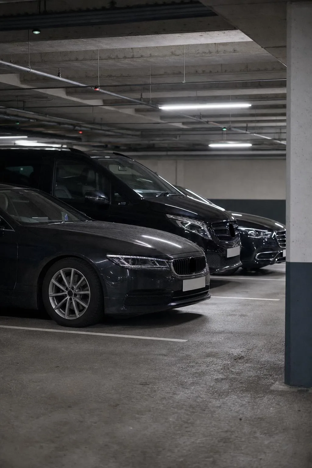 Three dark executive cars parked in a neat row in an underground car park.